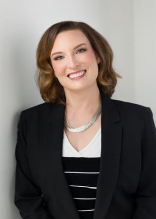 Nicole Eisdorfer smiling, wearing a black blazer and a layered silver necklace